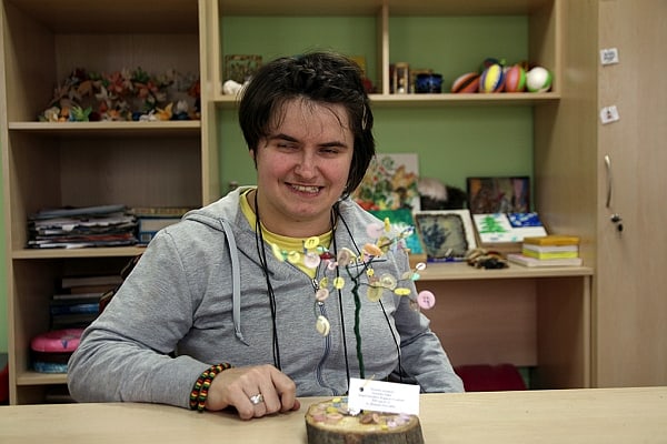 Dominika Dalka uśmiecha się do zdjęcia siedząc przy stolę przed swoim dziełem drzewkiem szczęścia.