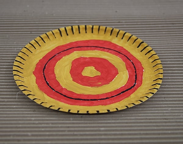 Talerz z “Tanganiki”. Rękodzieło z użyciem papierowego talerza pomalowanego w kolorowe wzory pomarańczowo żółto czarne.