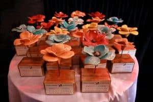 Na stoliku leżą statuetki z napisem: “Przystanek Talentowo”. Statuetki mają różnokolorowe kwiaty.