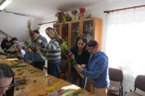 Ludzie trzymają w dłoniach kolorowe palemki. Stoją nad stołami z materiałami do ich konstruowania.