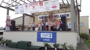 Grupa dzieci jest na scenie. Jedna z dziewczynek stoi i ma szeroko rozłożone ręce. Na górze wisi baner z napisem: “ Charytatywny maraton dobra”.