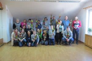 Grupa ludzi pozuje do zdjęcia. Niektórzy kucają inni stoją. W dłoniach ludzie mają kolorowe palemki.