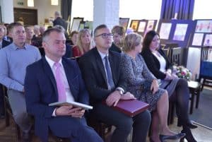 Ludzie siedzą na widowni. Są ubrani wizytowo. Ich twarze są zwrócone na przeciwko siebie.