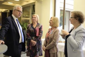 Ludzie stoją w grupie. Twarze mają zwrócone ku sobie. Niektórzy uśmiechają się.