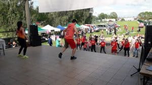 Na scenie jest dwójka osób- mężczyzna i kobieta. Przed nimi, na widowni grupa osób stoi, a niektórzy mają rozłożone ręce.