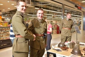 Dwóch mężczyzn w mundurach ściska się za ręce i śmieją się do obiektywu. Na stole leżą hełmy stare.