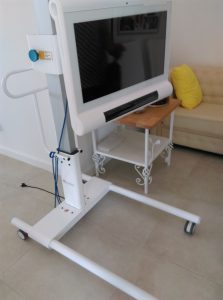 Urządzenie z monitorem stoi w pomieszczeniu. Obok niego po prawej stronie jest stolik, a za nim kanapa.