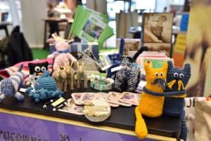 Na stole leżą różne zwierzęta z włóczki. Np. dwa koty - żółty i niebieski, które się przytulają lub niebieska ośmiornica.