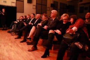 Na widowni siedzi grupa osób. Wszyscy patrzą przed siebie.