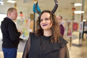 Kobeita w czarnym stroju ma rogi diałbła założone na głowie. Uśmiecha sie.