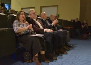 Ludzie siedzą na widowni. Klaszczą w ręce.