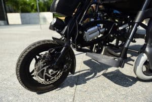 Na zdjeciu jest koło z wózka inwalidzkiego. W tle deptak.