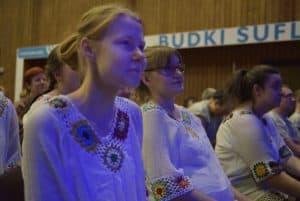 Osoby siedzą na krzesłach i patrzą przed siebie. Sa bokiem do obiektywu.