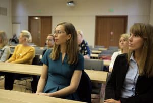 ludzie siedzą przy stołach. Ich twarze skierowane są na wprost.