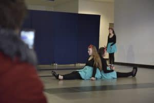 Dzieci są na środku sceny. Dwie dziewczynki siedzą i opierają sie plecami o siebie.