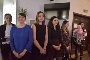 Ludzie stoją w grupie. Twarze są zwrócone przed siebie. Uśmiechają się.