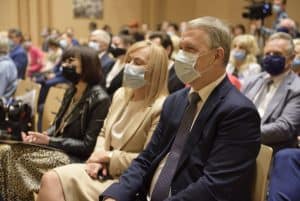 Grupa osób na widowni siedzi na krzesłach. Wszyscy patrzą w jednym kierunku.