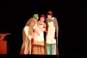 Na scenie stoją trzy kobiety. Są ubrane jak kobiety z wsi. Jedna z nich stoi bokiem do obiektywu.