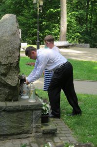 Mężczyzna pochyla się do zniczy. W tle drzewa parku.