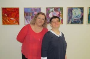 Kobiety stoją na tle ściany z kolorowymi zdjęciami. Uśmiechają sie do zdjęcia.