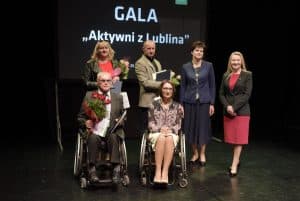 Osoby pozują do zdjęcia. Z przodu są dwie osoby na wózkach inwalidzkich, a z tyłu są cztery osoby. Na prezentacji za nimi jest napis: “ Gala. Aktywni z Lublina”.