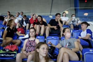 Mężczyźni i kobiety siedzą na trybunach. Są także dzieci.