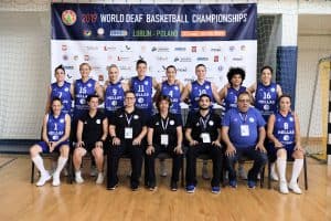 Kobiety i mężczyźni pozują do zdjęcia. Siedem osób z przodu siedzi na krzesłach, a osiem stoi z tyłu.