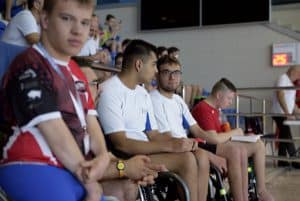 Grupa młodych mężczyzn na wózkach siedzi koło siebie. Dwóch z nich patrzy wprost w obiektyw.