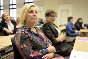 Kobiety siedzą przy stole. W tle inni ludzie przy stołach siedzący.