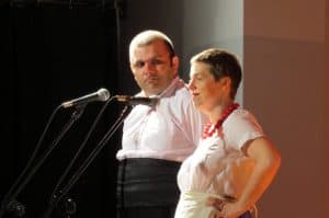 Kobieta z mężczyzną są na scenie. Przed nimi stoją mikrofony stojące.