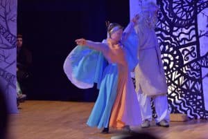 Kobieteta w długiej sukni jest na scenie. Pada na nią niebieskie swiatło.