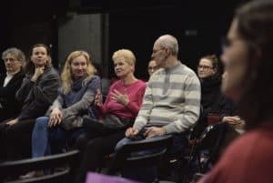 Na publiczności, jedna kobieta zaczyna gestykulować w kierunku siedzących obok niej ludzi. Niektórzy patrzą na nią. Jedna kobieta jest ukazana bokiem, lecz kontur jej twarzy jest niewyraźny.