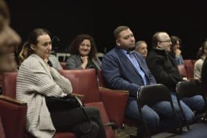 Grupa słuchaczy siedzi wygodnie w fotelach. Jedni są zasłuchani, inni się uśmiechają. Większość patrzy przed siebie.