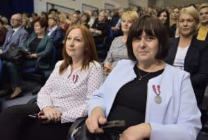 Kobiety siedzą wśród widowni. Mają one na sobie medale. Kobieta po prawej patrzy w obiektyw, a po lewej stronie pani patrzy przed siebie.