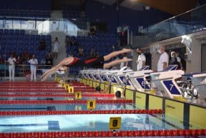 Uczestnicy zawodów skaczą do wody. Z tyłu są kibice.