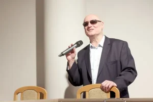 Mężczyzna w okularach przemawia do mikrofonu.