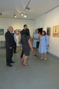 Starsi ludzi stoją w sali. Ich twarze są zwrócone ku sobie.