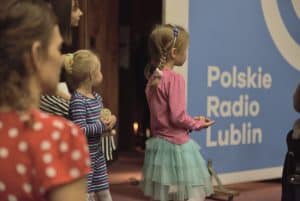 Napis Polskie Radio Lublin. Obok stoi dziewczynka. Za nią jest inne dziecko. Po lewej stronie stoi kobieta bokiem. Nie jest cała w kadrze.
