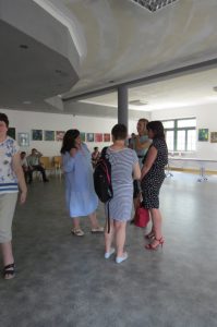 Ludzie stoją na środku sali. Są w grupie. Ich twarze są zwrócone ku sobie.