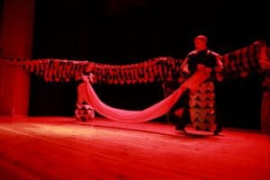 Na scenie stoi mężczyzna i trzyma rozciągnięty materiał. Za nim jest smok.