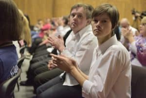 Osoby siedzą obok siebie. Kobieta i mężczyzna patrzą prosto w obiektyw.