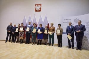 Mężczyźni i kobiety pozują do zdjęcia. W dłoniach trzymają dyplomy. Za nimi są flagi oraz godło Polski.