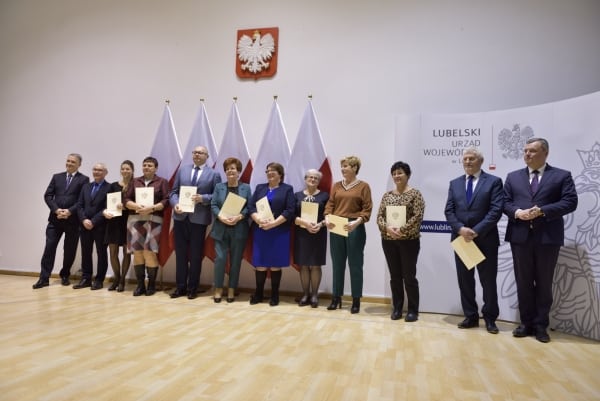 Mężczyźni i kobiety pozują do zdjęcia. W dłoniach trzymają dyplomy. Za nimi są flagi oraz godło Polski.