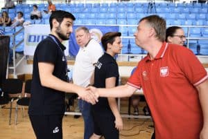 Dwoje męzczyzyn podaje sobie ręce. Są na boisku. Ich twarze są zwrócone ku sobie.