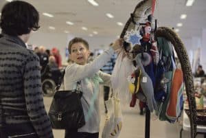 Kobieta wyciąga rękę do wieszaka z rękodziełami i pluszakami kolorowymi. Kobieta stoi naprzeciwko mężczyzny, którego twarz jest skierowana w jej stronę.