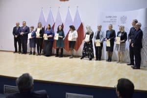 Osoby pozują na scenie do zdjęcia. Są to kobiety i mężczyźni, którzy trzymają dyplomy.