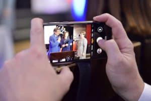 Na zdjęciu jest smartfon. Osoba robi zdjęcia ludziom na scenie.