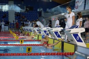 Zawodnicy ukończyli przepłynięcie. Na zewnątrz są osoby ubrane na biało. KObieta trzyma stoper.