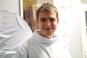 Mężczyzna przebrany za anioła uśmiecha się do obiektywu. Ma na sobie skrzydła.