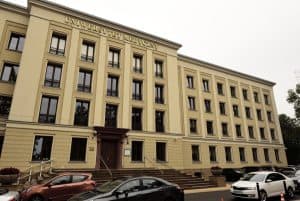 Na zdjęciu jest budynek uniwersytetu medycznego. Przed nim stoją auta.